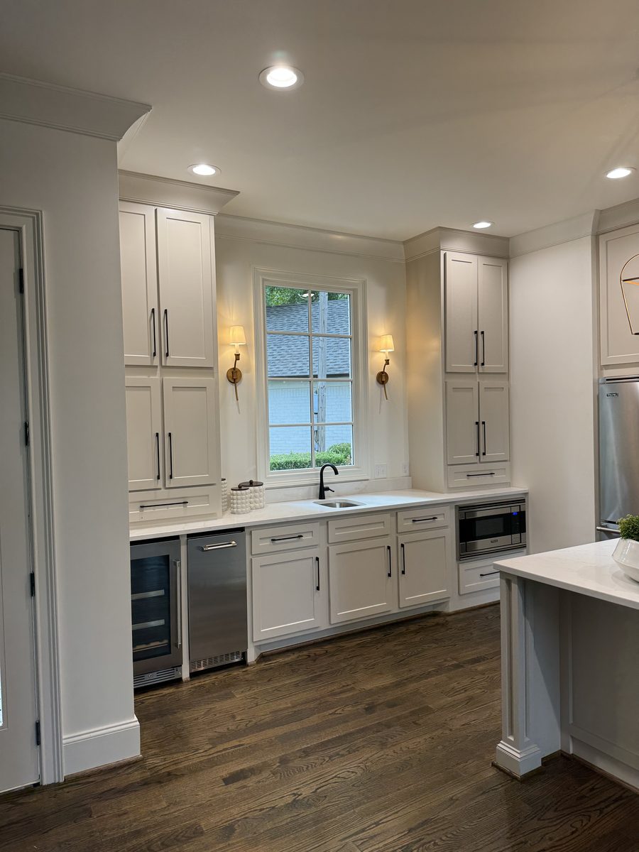 Bright white kitchen with warm sconce lighting and paneled hood